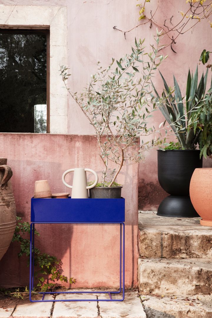 Blumentöpfe für draußen: Hier sehen Sie die Plant box aus Metall in Kobaltblau von Ferm Living, gefüllt mit Terrakotta-Töpfen, einer Vase und einer großen Pflanze mit grünen Blättern.