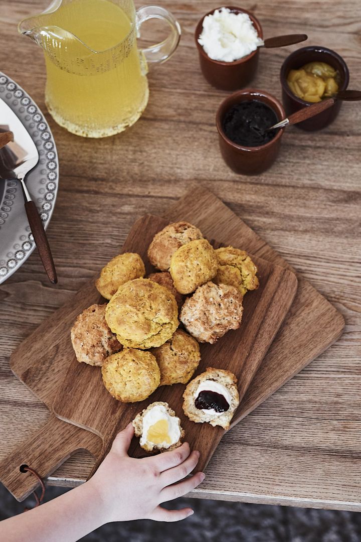 Die Gäste werden mit goldenen Scones verwöhnt, die auf einem Walnuss-Schneidebrett von House Doctor serviert werden. 