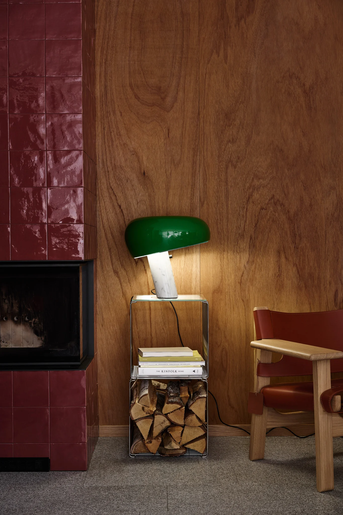 Ein Schlafzimmer mit cremefarbener gemusterter Bettwäsche, einer plissierten Lampe auf einem Holznachttisch und einem hohen Spiegel vor Blättertapete.