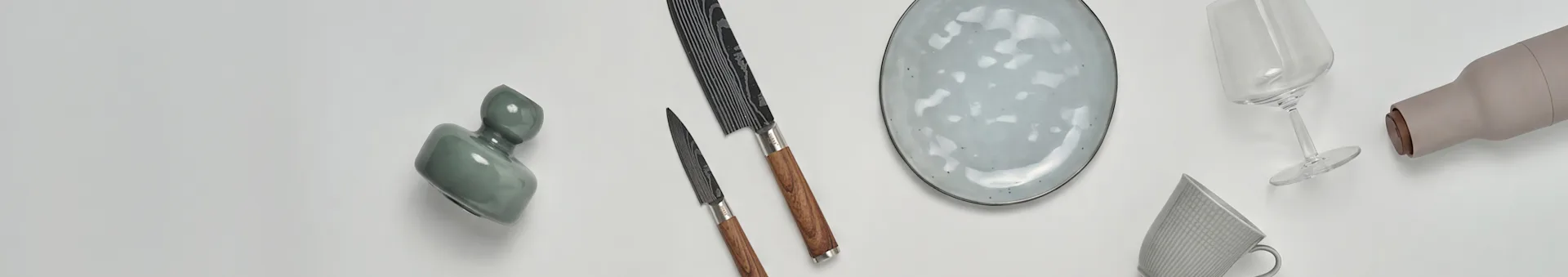 Verschiedene Küchen- und Essartikel, darunter eine grüne Vase, zwei Messer, ein gesprenkelter Teller, ein Weinglas, eine beige Flasche und eine gemusterte Tasse.