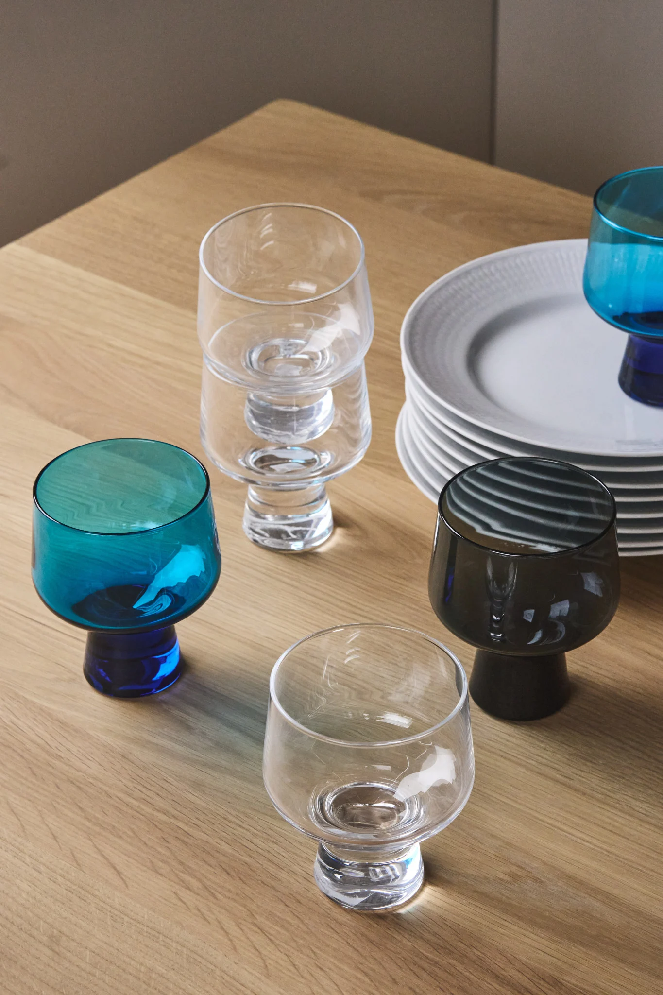 Hier sehen Sie eine Sammlung von Gläsern aus der Solare-Kollektion von Iittala zusammen mit einem Stapel weißer Teller. 