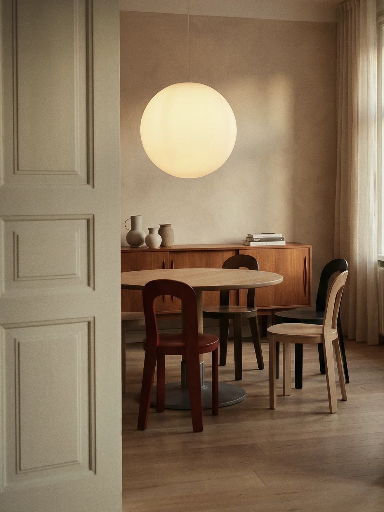 Ein modernes Esszimmer mit einem runden Holztisch, verschiedenen Stühlen, einer großen kugelförmigen Pendelleuchte und einem Sideboard mit Vasen.