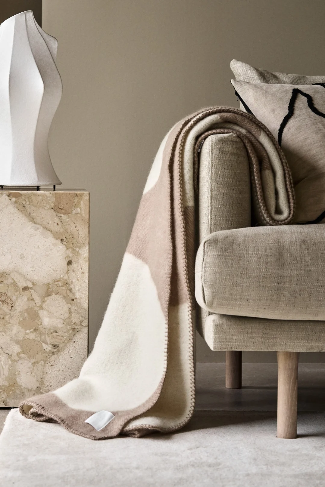 Die beigefarbene Leaf Decke von Sagaform liegt über der Lehne einer Couch.