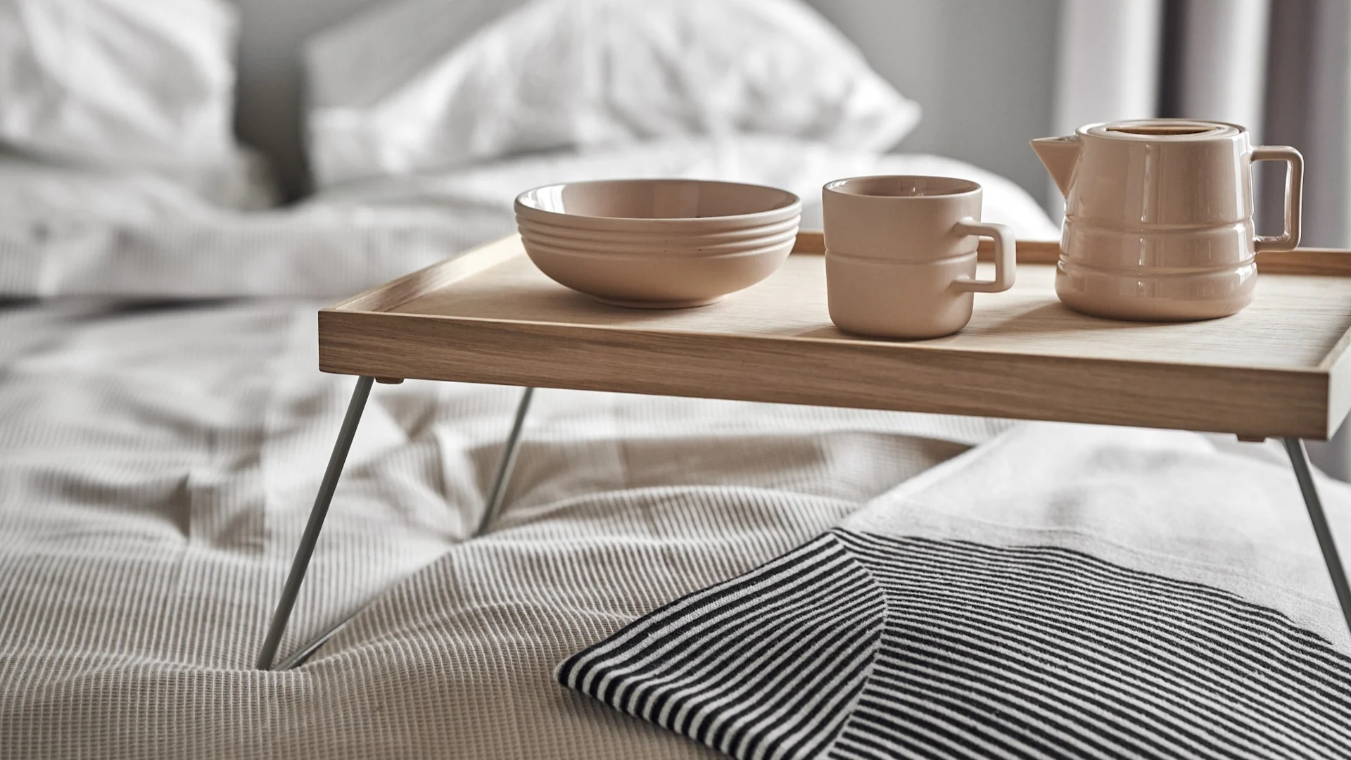 Lagom bedeutet auch, entspannt in den Tag zu starten. Hier stehen eine Tasse, eine Kanne und eine Schüssel aus der Lines-Kollektion von NJRD auf einem Frühstückstablett im Bett.