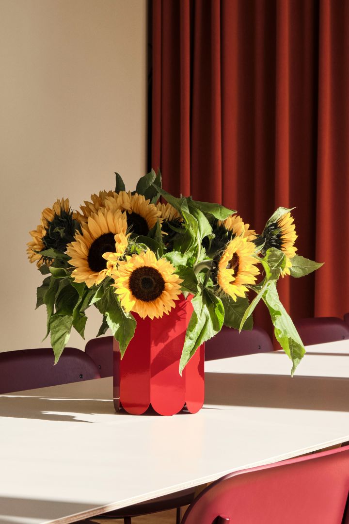 Rote Elemente gehören zu den stärksten Tönen der skandinavischen Wohntrends 2024 und sind hier in der verspielten, mit Sonnenblumen gefüllten Vase Arcs in Rot von HAY vertreten.