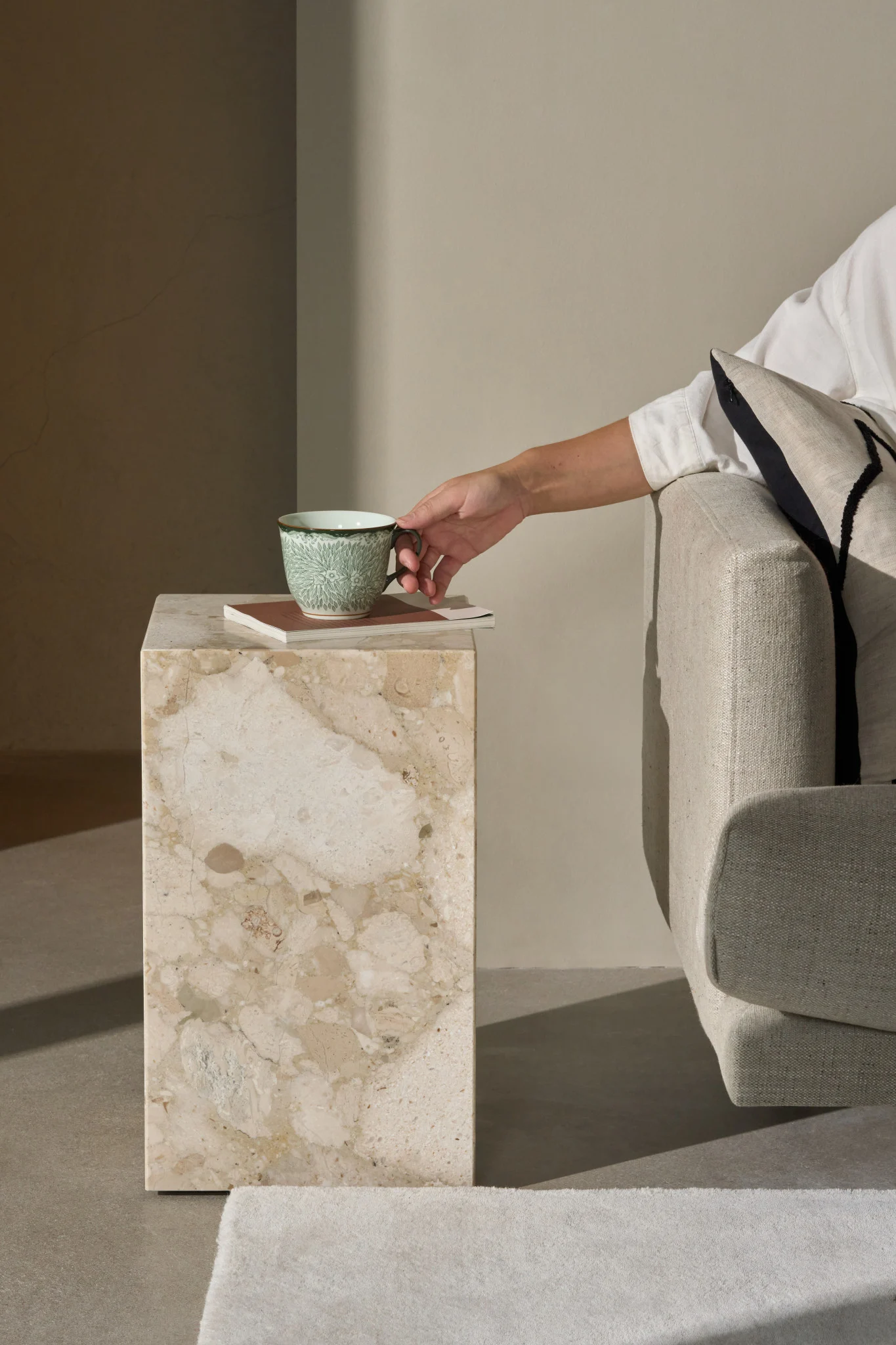 Hand greift nach einer grünen gemusterten Tasse auf einem Marmor-Beistelltisch neben einem Sofa.