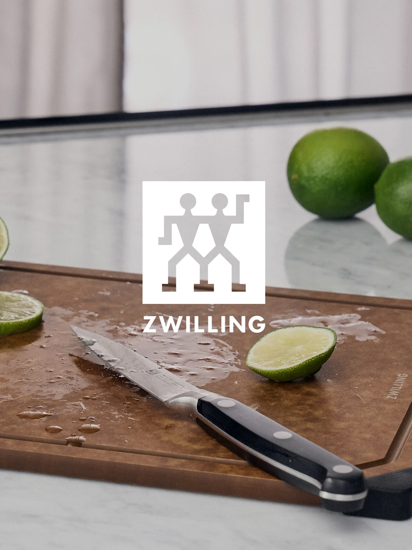 ZWILLING-Logo über einem Schneidebrett mit Messer, geschnittener Limette und ganzen Limetten.