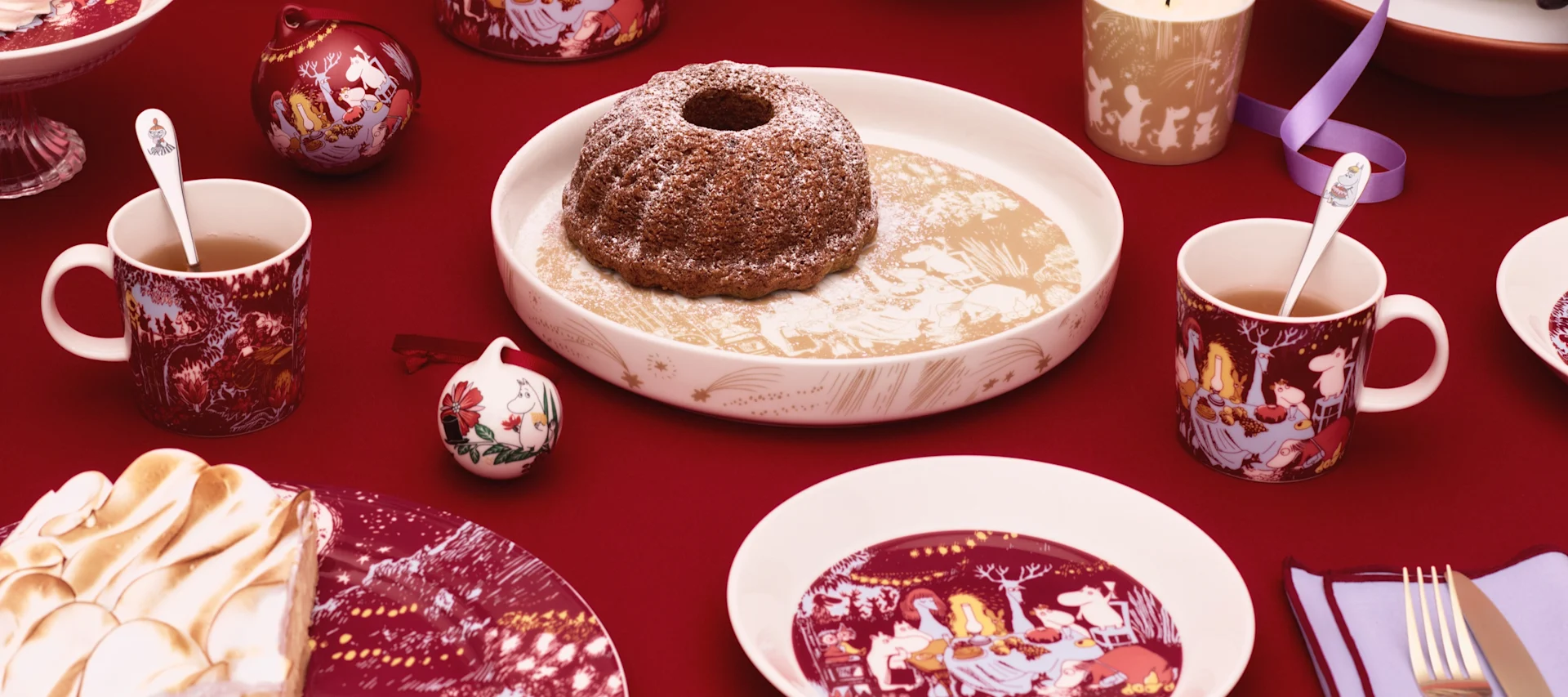 Verschiedene Mumin-Tassen von Moomin Arabia stehen draußen auf einem Tisch, daneben eine Stempelkanne.