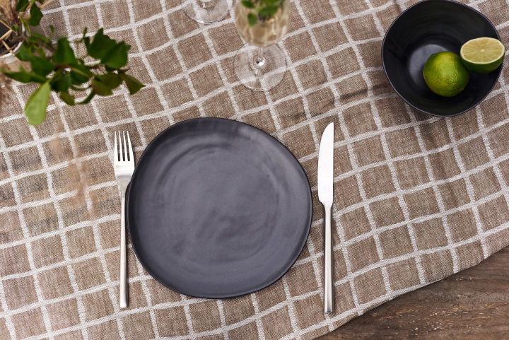 Ein einfach gedeckter Tisch mit Steingutgeschirr und stilvollem Besteck von Scandi Living auf einer karierten Tischdecke. 