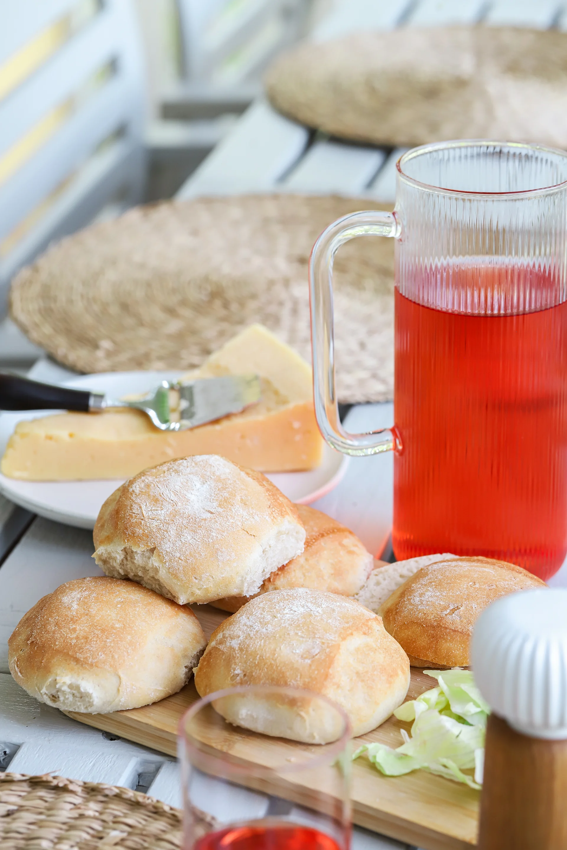 Das Bild zeigt frisch gebackene Brötchen, gestapelt auf dem Naturschneidebrett aus Bambus von Sagaform. Im Hintergrund sind die Saga-Karaffe und ein Trinkglas zu sehen.
