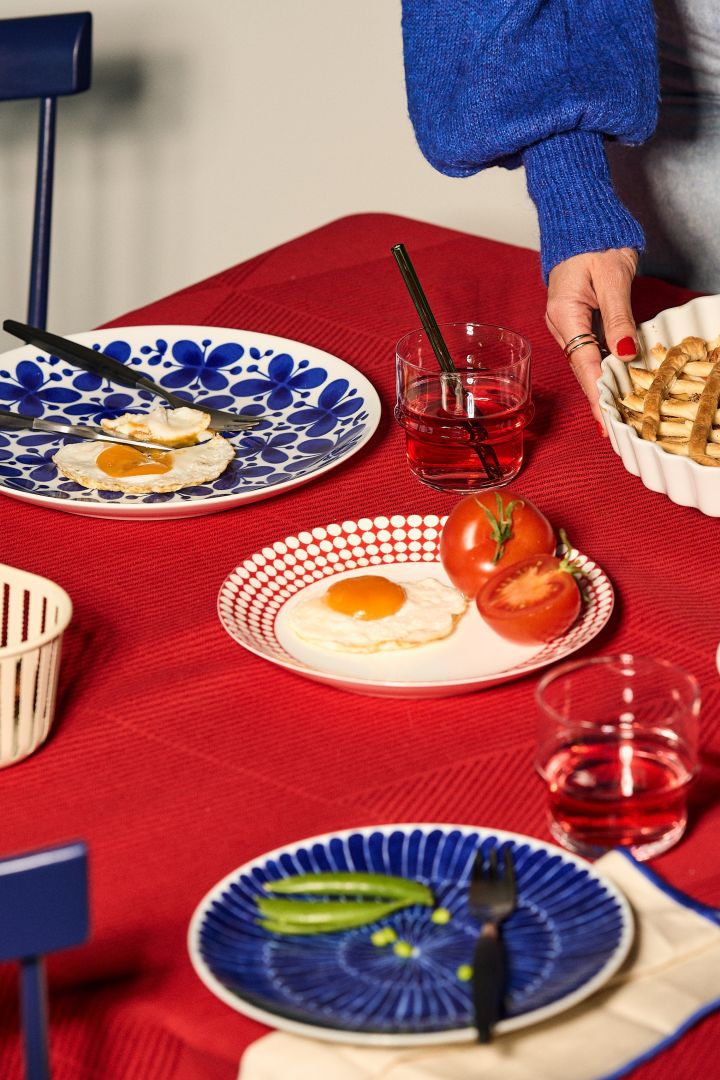 Farbtrends 2024: Die Trendfarben des Jahres sind Blau und Rot, welche Sie hier auf einem gedeckten Tisch in Form einer roten Tischdecke von NJRD und Geschirr aus der Mon Amie-Serie von Rörstrand sehen.