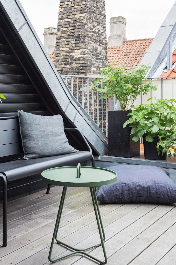 Der On the move Tisch von Cane-line, hier auf einem Balkon stehend, besticht nicht nur mit seiner grünen Farbe, sondern auch mit seiner Multifunktionalität und passt somit hervorragend in die Gartenmöbel-Trends 2025.