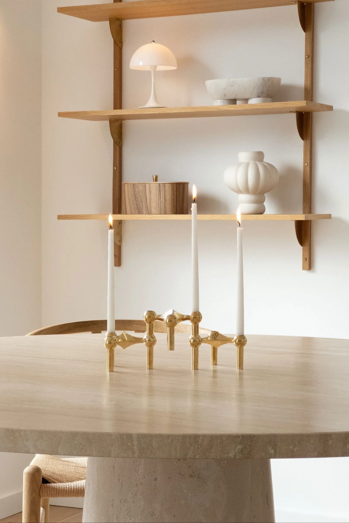 Ein goldener Kandelaber mit drei brennenden Kerzen auf einem runden Tisch, dahinter Regale mit Deko-Objekten.