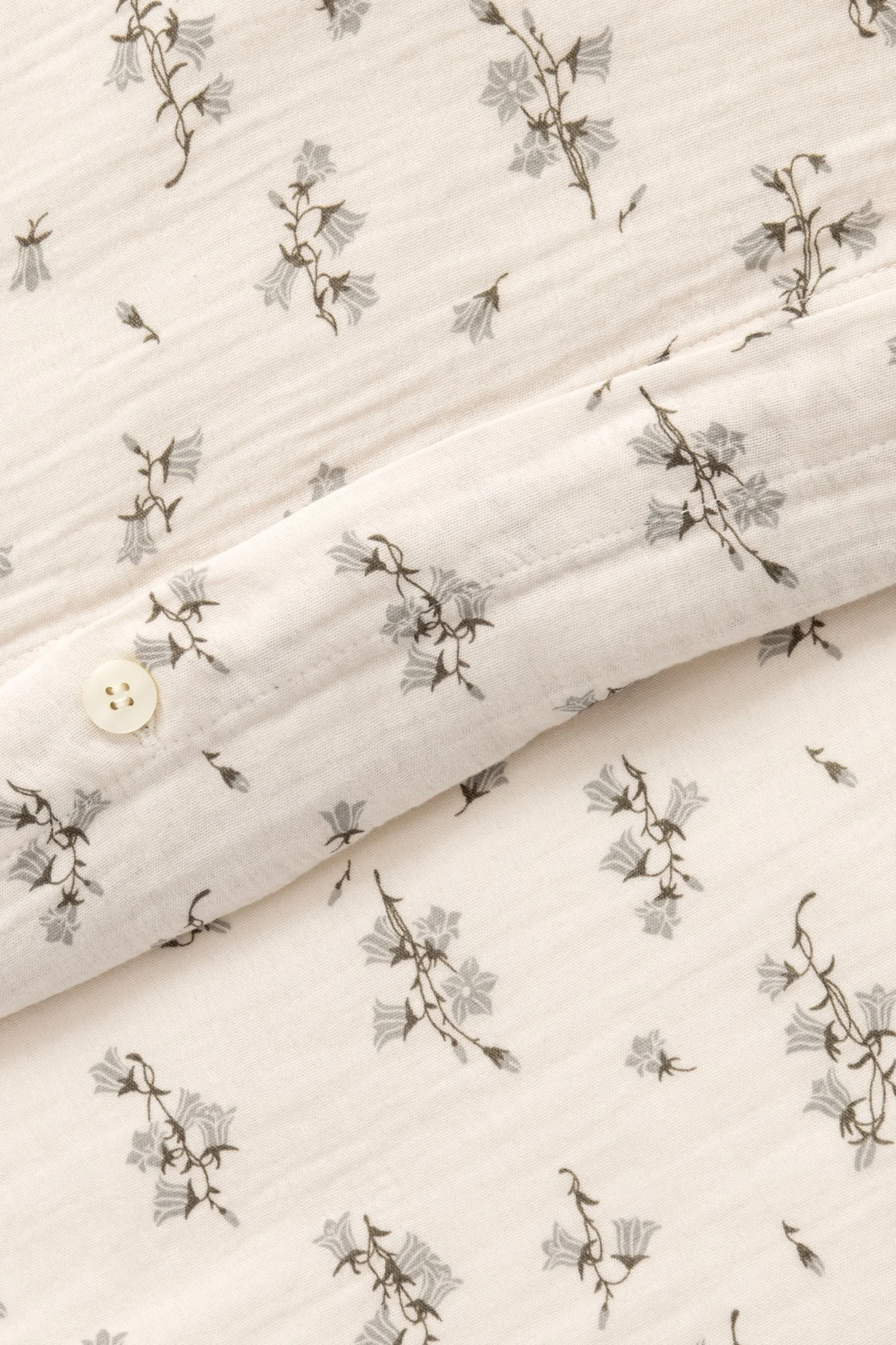 Nahaufnahme von cremefarbenem Stoff mit grauem Glockenblumenmuster und einem weißen Knopf.