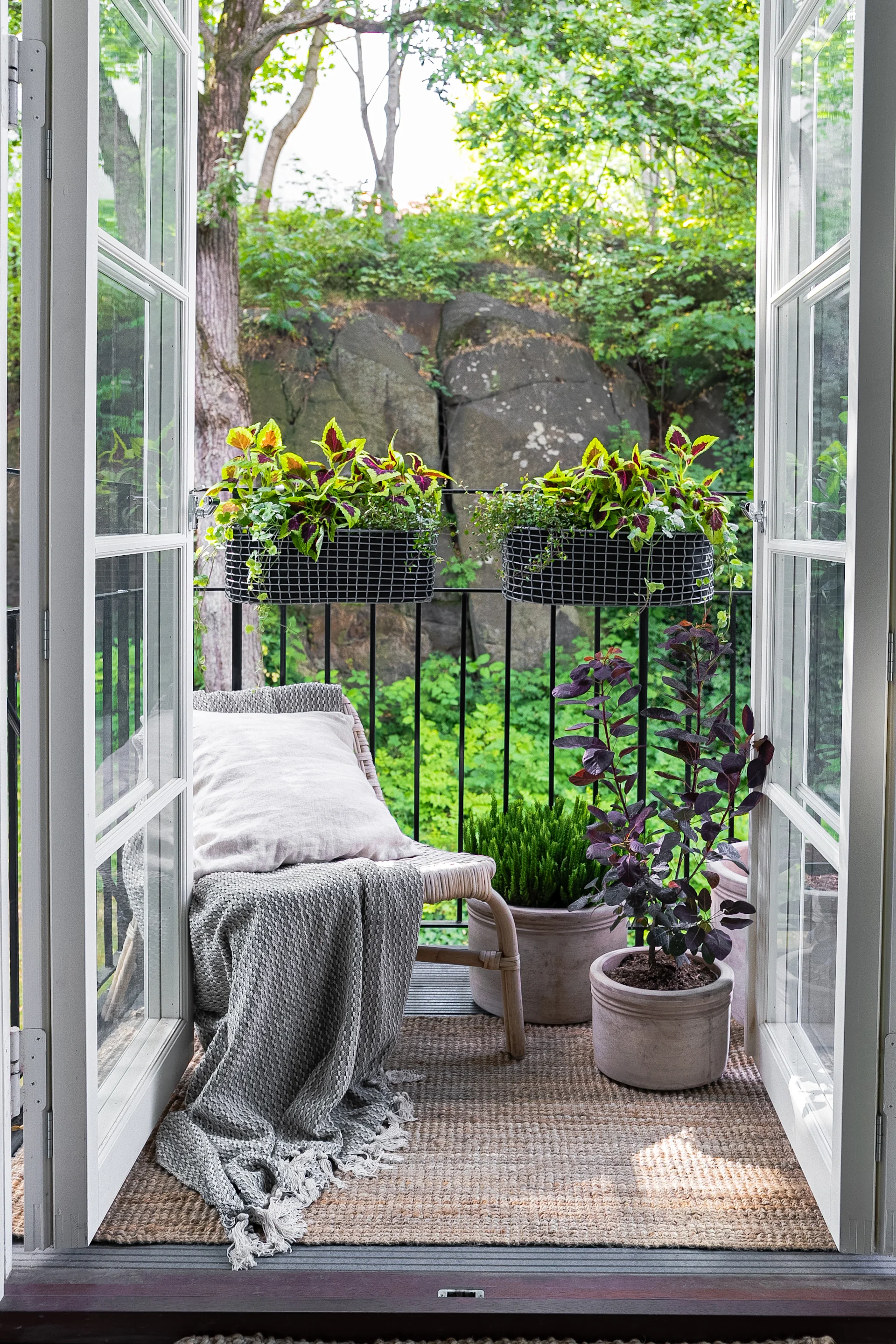 Ein kleiner, gemütlich eingerichteter Balkon mit einem Sessel und mehreren Pflanzen, unter anderem im Korbo Balkonkorb.