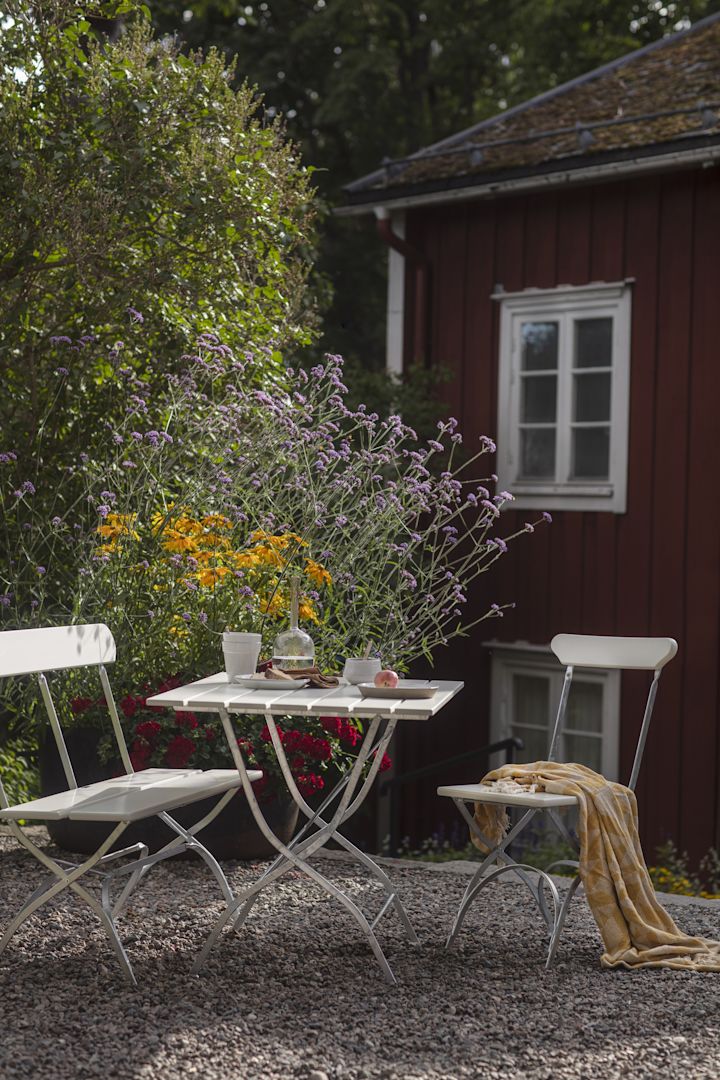 Grythyttan: Die Biergarten-Serie, bestehend auf zwei Stühlen und einem Tisch in Weiß, steht vor einem roten schwedischen Holzhaus.