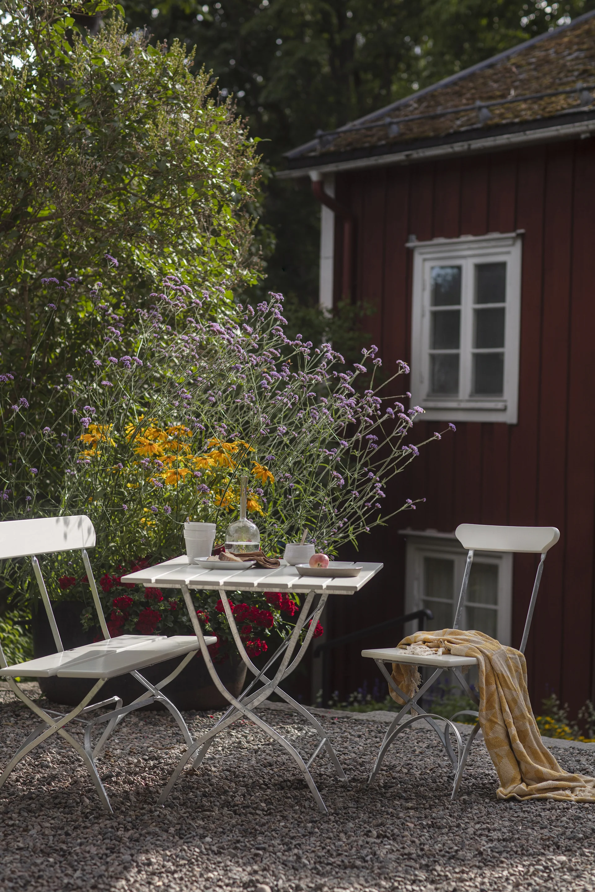 Grythyttan: Die Biergarten-Serie, bestehend auf zwei Stühlen und einem Tisch in Weiß, steht vor einem roten schwedischen Holzhaus.