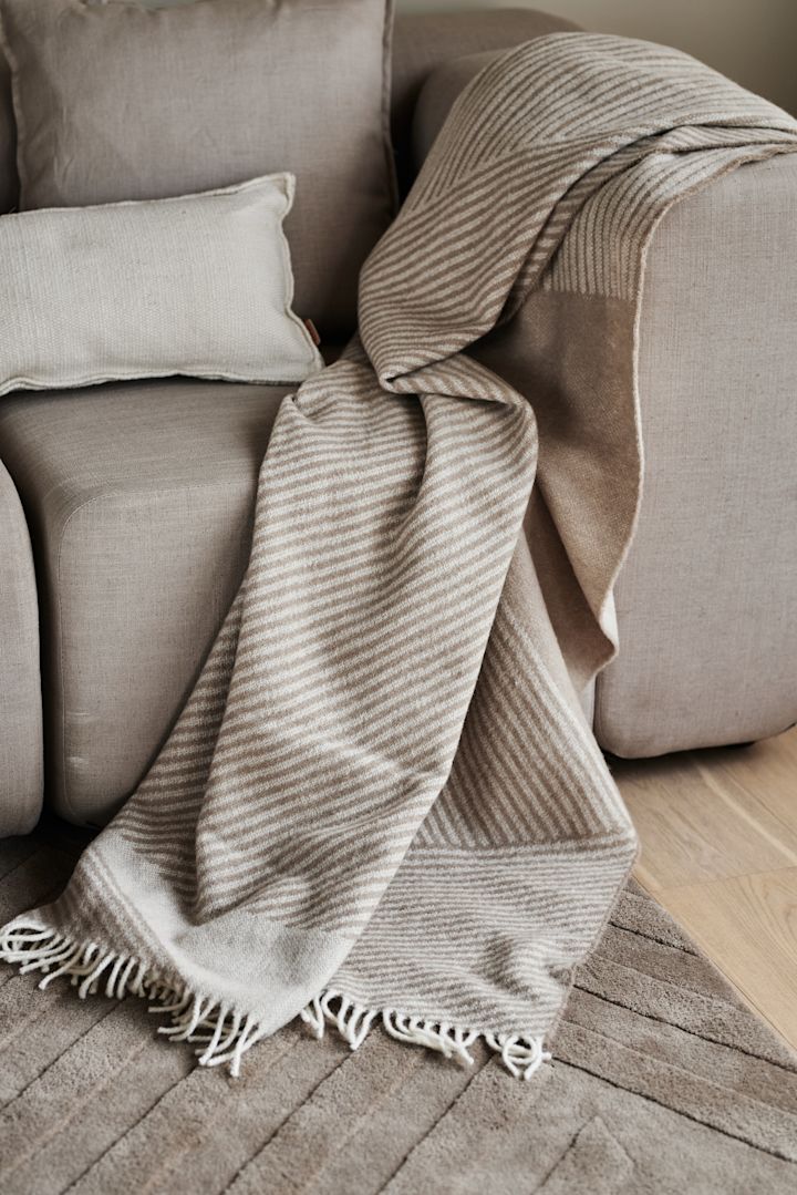 Die kuschelige beigefarbene Decke Stripes von NKRD liegt auf einer Couch.