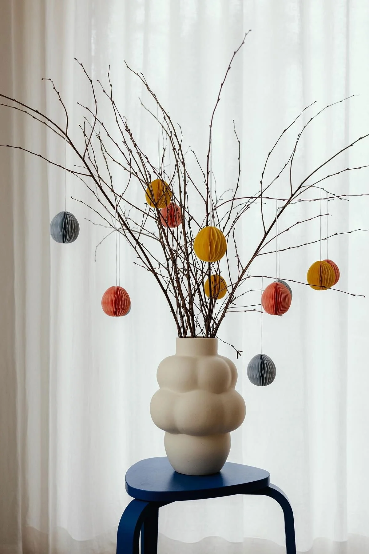 Ein Osterstrauch auf einem Hocker, in der weißen Balloon 04 Vase von Louise Roe, dekoriert mit bunten Brooding Papiereiern von Scandi Living im Zuhause von @applaudden.