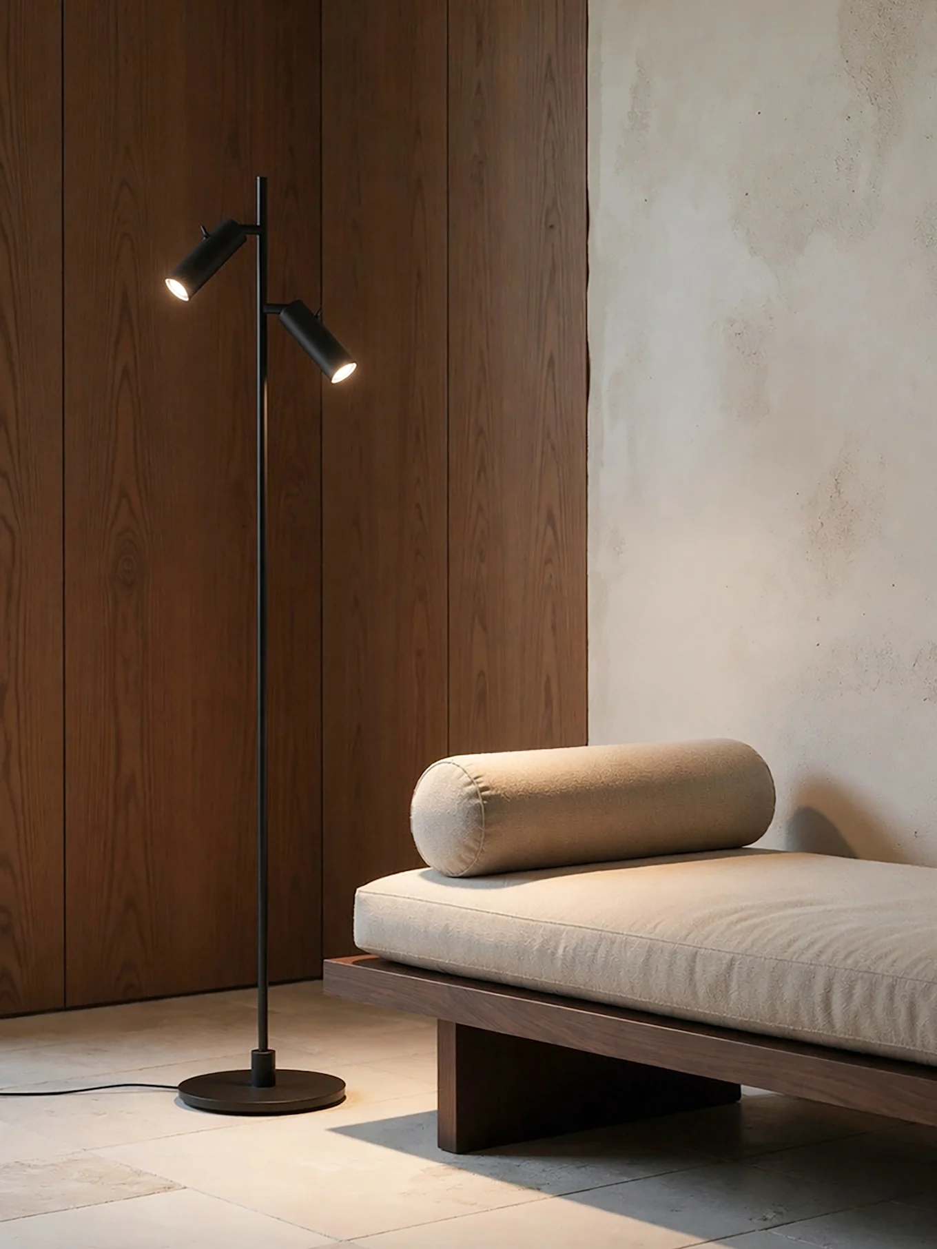 Ein modernes Zimmer mit einer schwarzen Stehlampe mit zwei Lichtern neben einem Holz-Daybed mit hellem beigem Kissen und Nackenrollen.