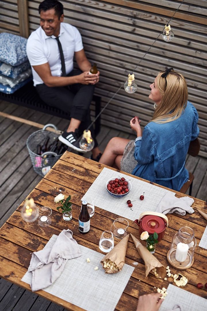 Ein Sommerfest auf der Dachterrasse, bei dem Snacks und Getränke in einer entspannten Atmosphäre im Hygge-Stil genossen werden können. 