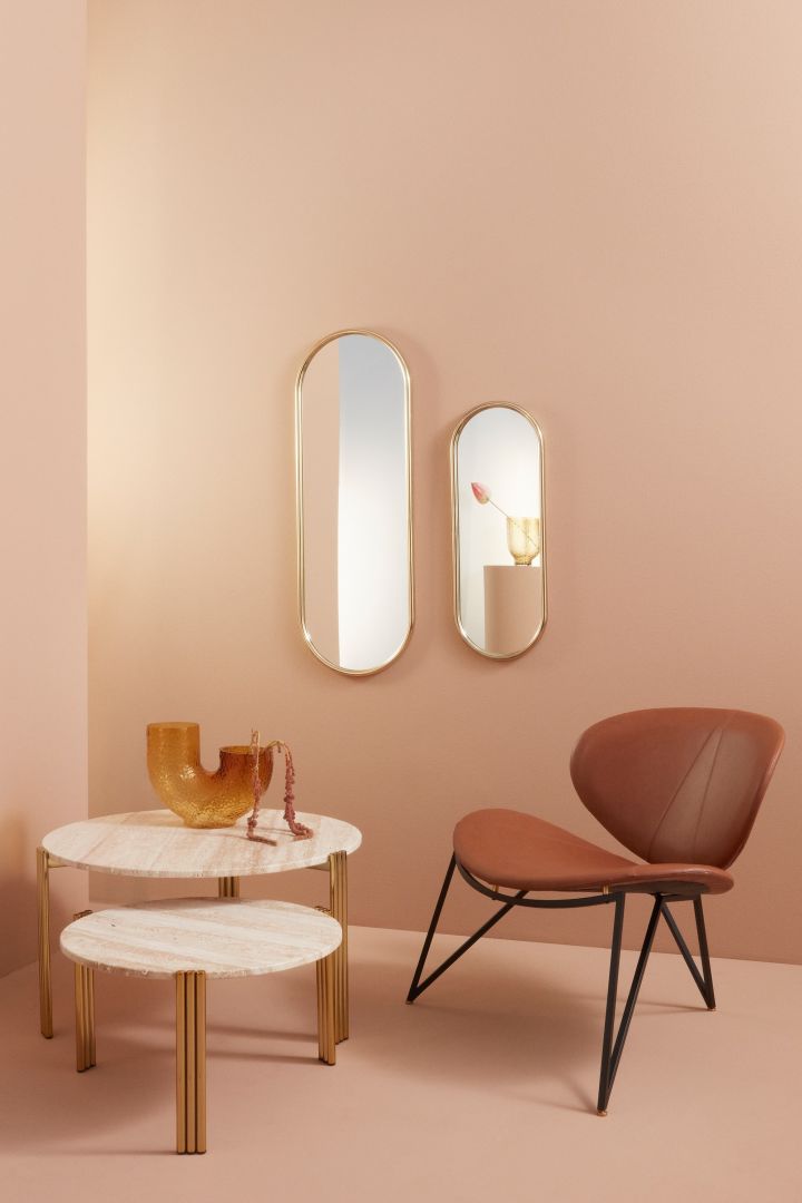 Stylisches Wohnzimmer in Pfirsichtönen an den Wänden, Spiegel mit Messingkanten und ein schöner Ledersessel – alles aktuelle Wohntrends für 2023.