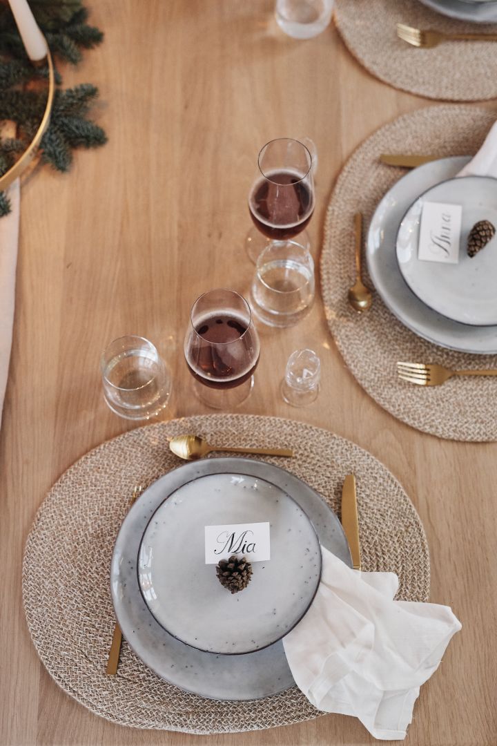 Eine weiße Weihnachtstischdekoration mit einem Gedeck bestehend aus rustikalen Steinzeug Tellern goldenem Besteck und einer weißen Leinenserviette.