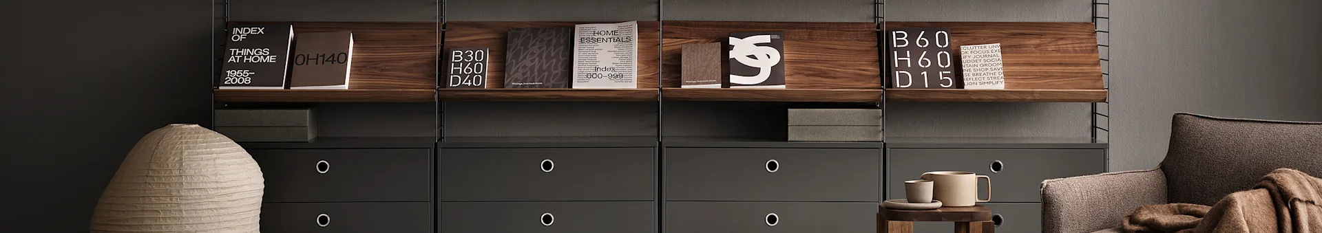 Modernes Regalsystem mit dunklen Holzregalen, grauen Schubladen, Büchern, einer hellen Vase, einem braunen Sessel und Keramikaccessoires.