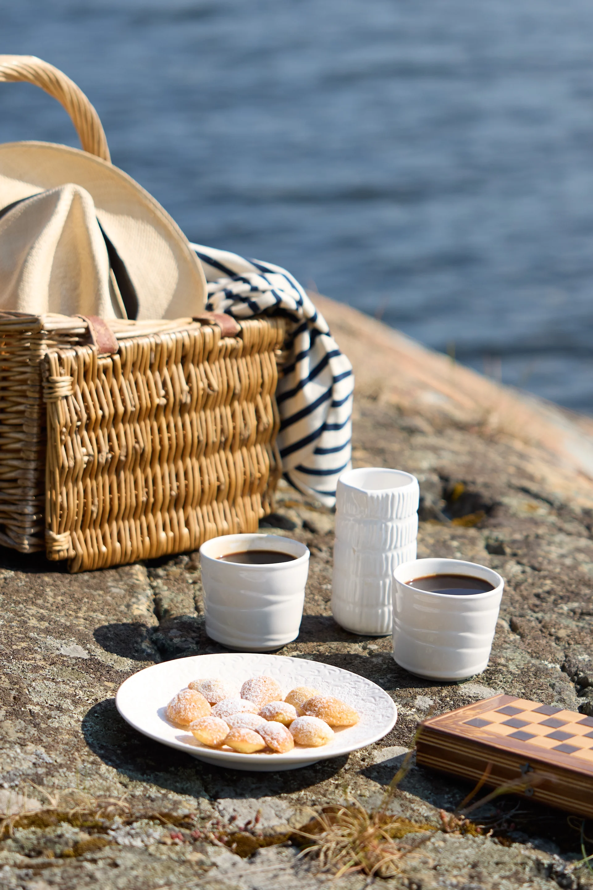Ein Picknick auf felsigem Gelände am Wasser, mit Kaffee, Gebäck und einem Schachspiel.