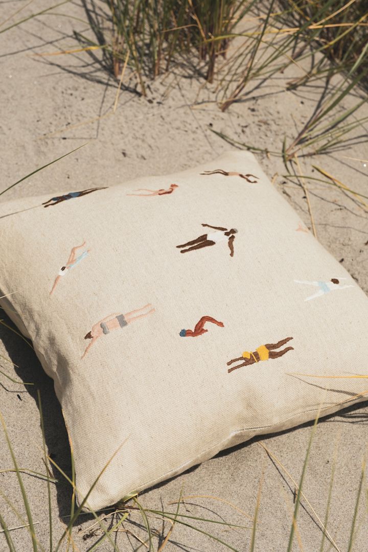 Ein Kissen mit dem Swimmers Kissenbezug von Fine Little Day liegt am Strand im Sand.