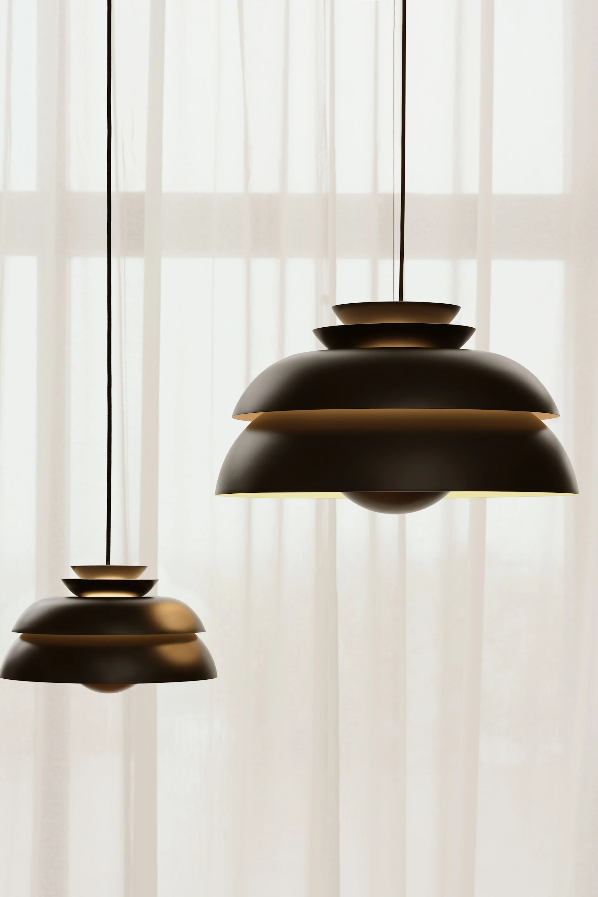 Die schwarze Concert-Pendelleuchte in Schwarz von Fritz Hansen hängt vor einem Fenster mit Gardinen.