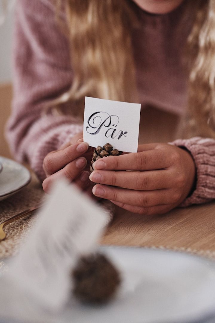 In dieser weißen Weihnachtstischdekoration werden Tannenzapfen mit handgeschriebenen Namenskärtchen für die Tischdekoration verwendet.