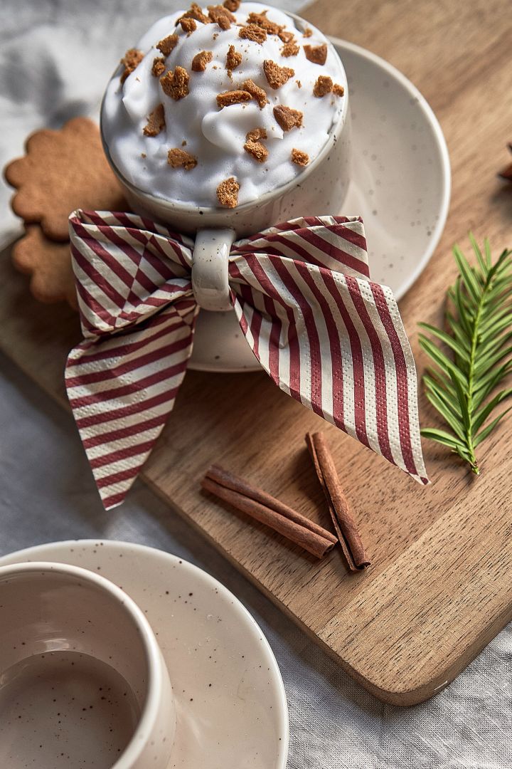 Einfache Weihnachtscocktails: Dekorieren Sie Ihre Heiße Schokolade oder Ihren Kaffee mit einer Sahnehaube, zerbröselten Lebkuchen und gemahlenem Zimt. Zum Servieren können Sie eine Serviette als Schleife im Henkel drapieren.