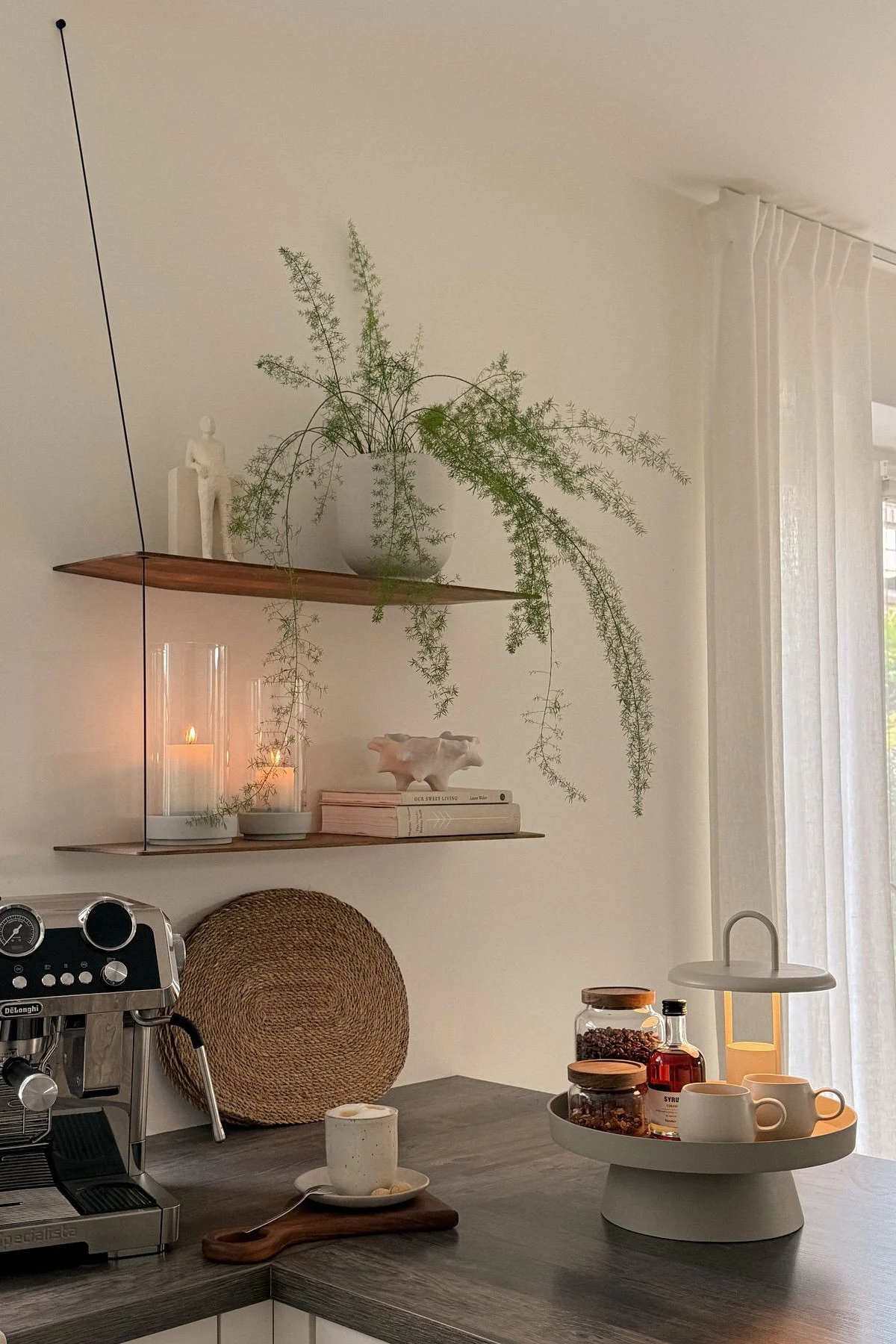 Eine Heimkaffeestation mit Maschine, Tasse, zwei Regalen mit Pflanze und Kerzen, sowie einem Tablett mit Kaffeezubehör und Lampe.
