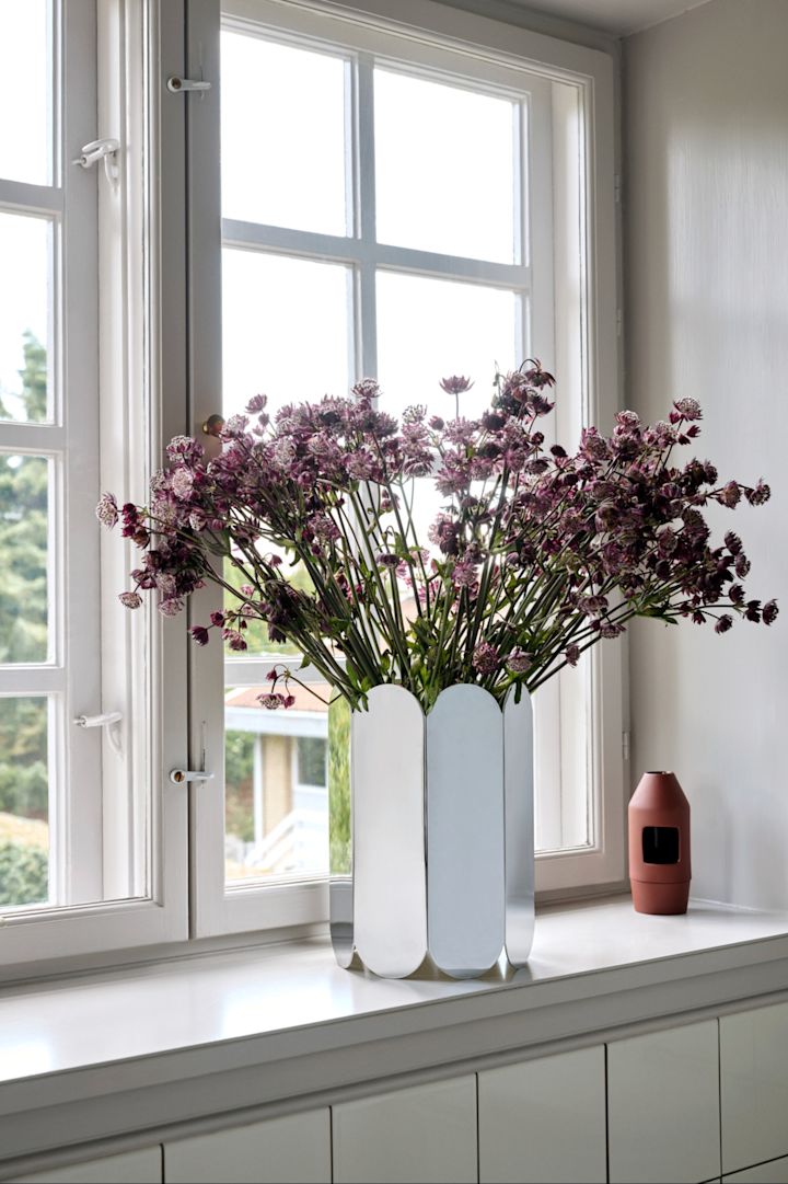 Eine dekorierte Fensterbank mit der Arc Vase mit lilafarbenen Blumen.