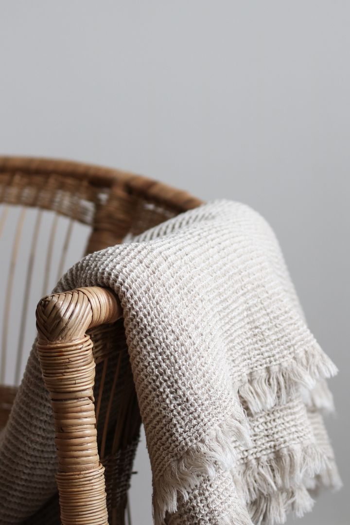 Die beigefarbene Calma Decke aus Strick hängt locker über einem Küchenstuhl. 