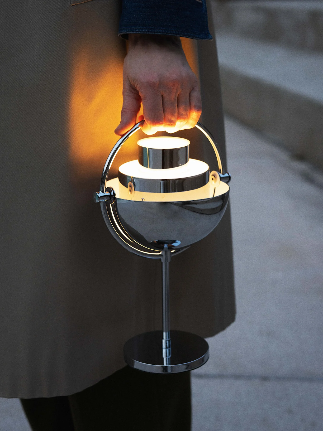 Hand hält eine leuchtende, moderne tragbare Chromlampe.