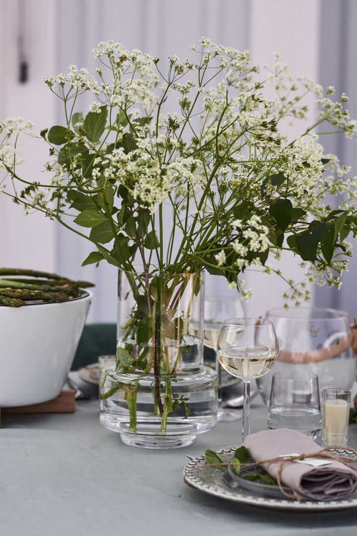 Ein Strauß Gartenblumen in einer hohen Klarglasvase aus der Ro Collection steht auf dem Tisch der Gartenparty. 