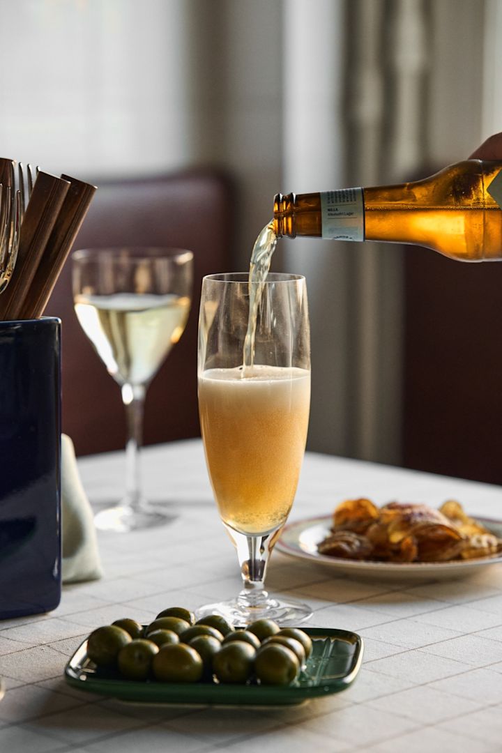 Erfahren Sie, welches Bierglas zu welchem Bier passt: Hier sehen Sie, wie ein Bier in das Chateau-Bierglas von Kosta Boda eingeschenkt wird, mit einem Teller Oliven daneben.