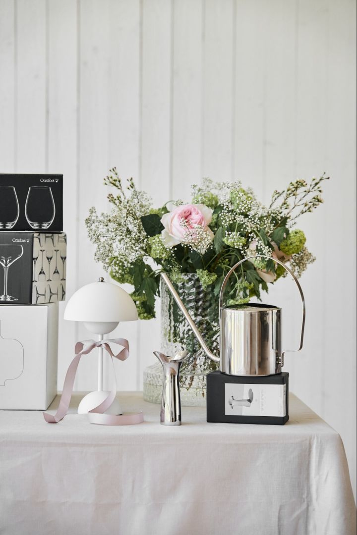 Lassen Sie sich von unseren einzigartigen Hochzeitsideen inspirieren! Hier sehen Sie eine Gießkanne aus rostfreiem Stahl von Stelton und eine Vase von Georg Jensen auf einem Tisch für Hochzeitsgeschenke. 