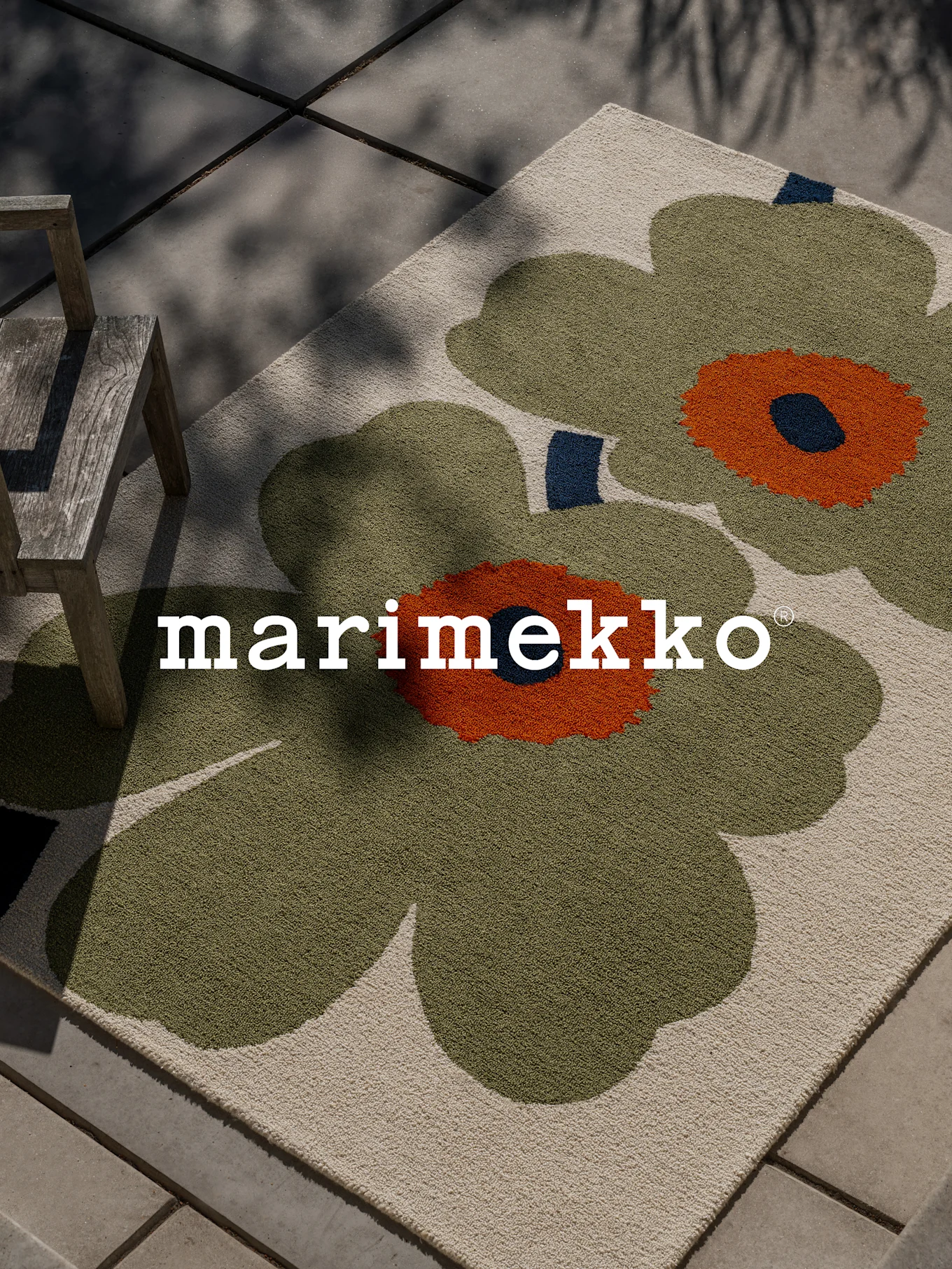 Marimekko Teppich mit großem grünem und orangefarbenem Blumenmuster auf einer Terrasse mit Holzstuhl.