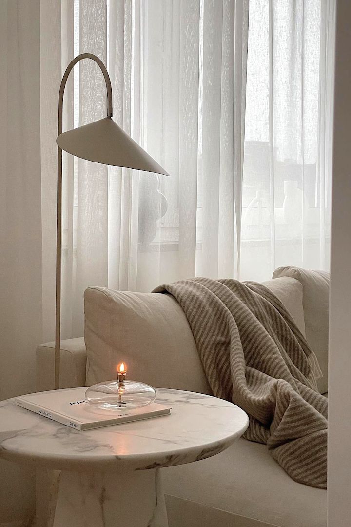 Das Wohnzimmer in Beige von @helenas.hem mit einem marmornen Beistelltisch, einer beigen Couch mit der Stripes Wolldecke von NJRD und der beigefarbenen Stehlampe Arum von Ferm Living.