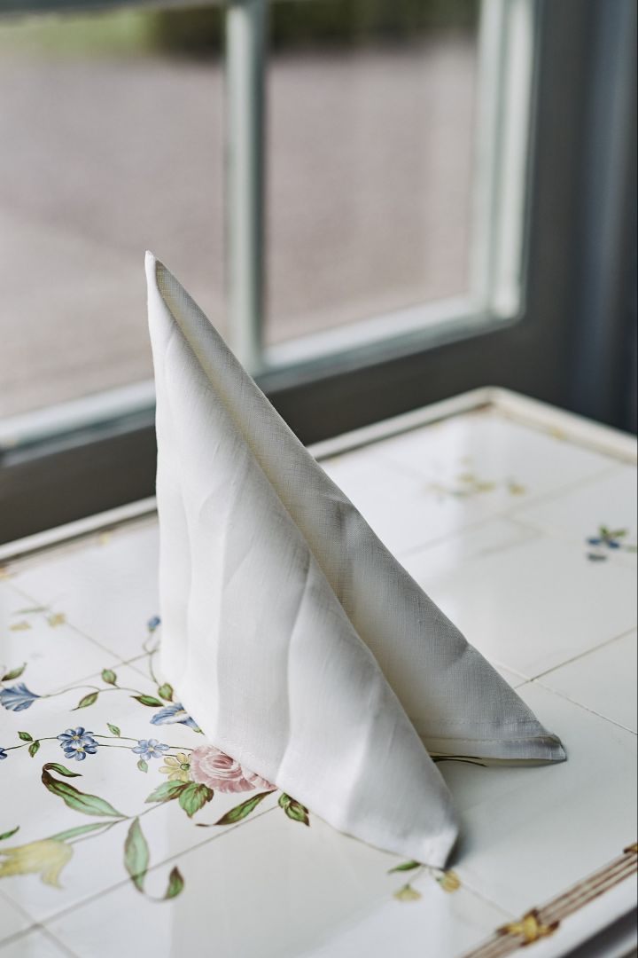 Eine klassische und einfache Serviettenfaltung in Form eines Segels mit einer weißen Serviette.
