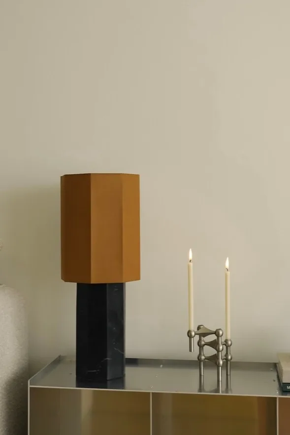 Moderne Tischlampe mit sechseckigem braunem Schirm und schwarzem Marmorsockel, neben einem modularen Kerzenhalter aus Silber mit zwei brennenden weißen Kerzen.