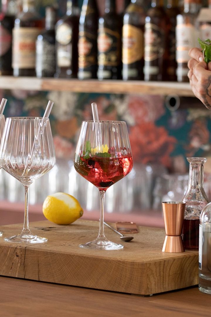 Ein alkoholfreier Cocktail im Feel Good G&T Glas von Nachtmann steht auf einem Holzbrett vor einer Bar.