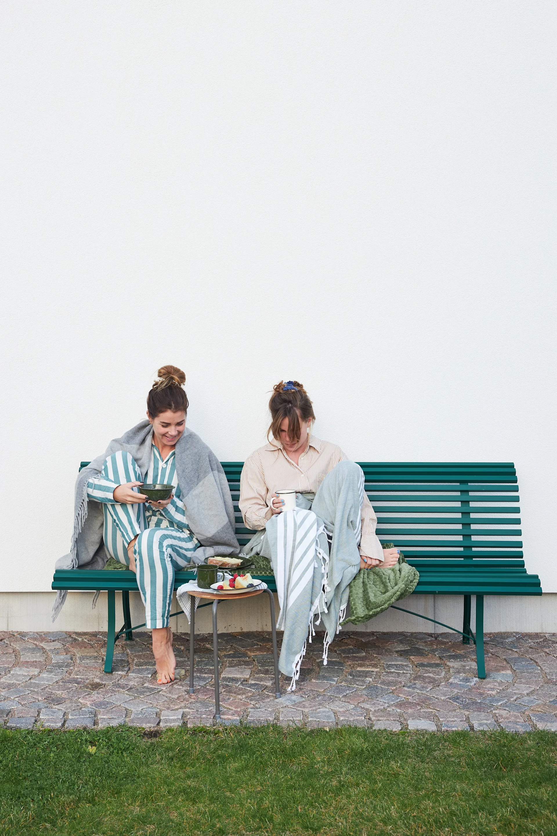 Fika: In Schweden ist Fika mehr als eine Kaffeepause, hier sitzen zwei Frauen entspannt mit Kaffee und Kuchen draußen auf einer Bank.