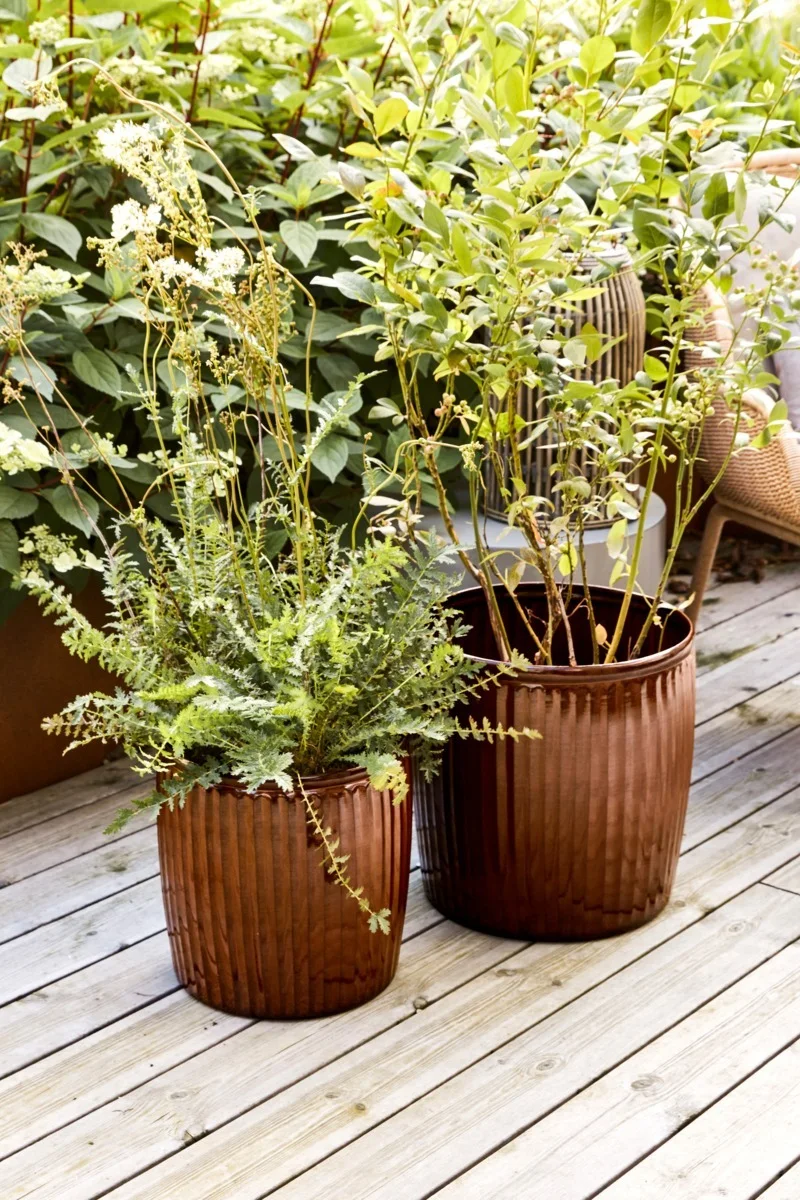 Brauntöne eignen sich sehr gut für einen Boho-Balkon. Hier sehen Sie die zwei Groove Blumentöpfe von House Doctor mit Blumen darin auf einem Balkon stehen.