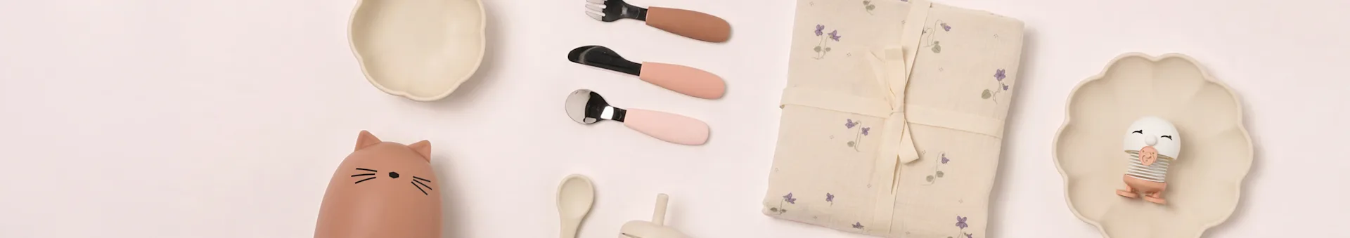 Baby-Essgeschirr-Flachlage: beige Teller, Katzenflasche, rosa Besteck, geblümte Decke, Eier-Spielzeug.